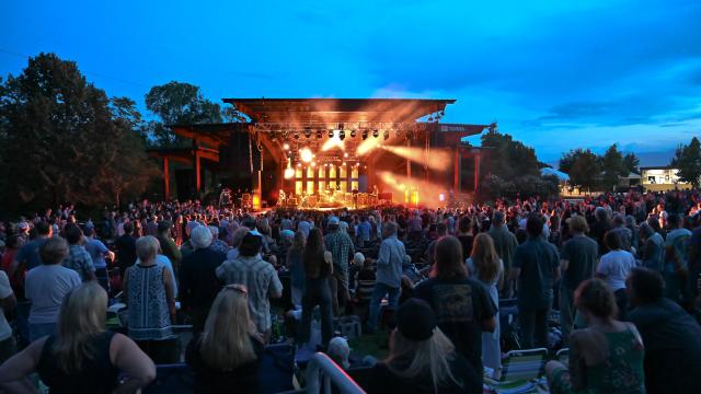 Crowd of people at dusk watching a brightly lit stage with a cool late evening sky