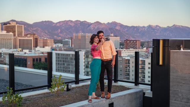 Couple standing and taking a selfie on the roof at Van Ryder with Salt Lake City Skyline and wasatch mountains in the background