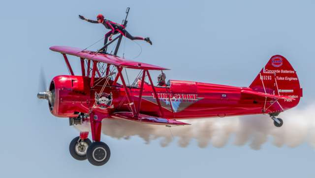 a person wingwalking on a red biplane while it is in flight