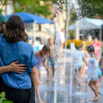 couple embracing as they watch kids splash in a fountain