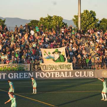Vermont Green FC players on Virtue Field at sunset with the bleachers in the background.
