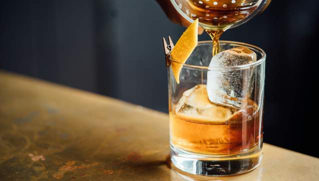 A glass of whiskey on the rocks with a twist of orange peel, capturing the moment liquid is poured over ice.
