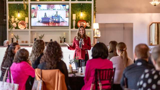 A woman speaks in front of a group of people sitting at tables.
