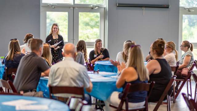 Numerous people meeting indoors seated at multiple tables