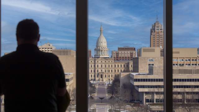 Person looking out a window at the Michigan State Capitol Building