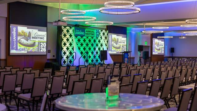 A ballroom set up with tables and chairs with the Choose Lansing branding