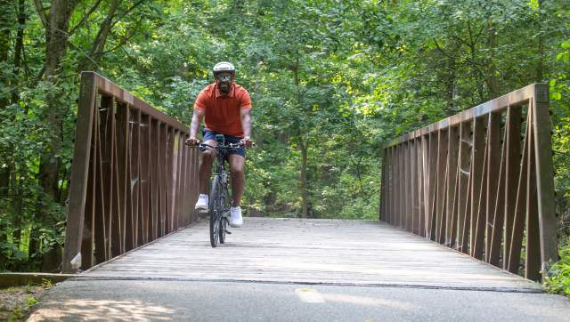 A man riding his bike across a bridge on the Lansing River Trail.