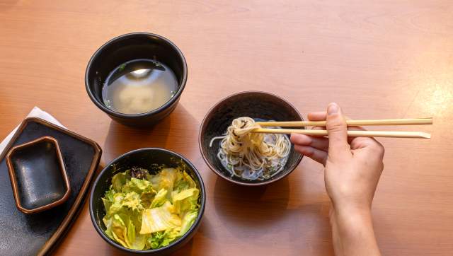 A person's hand using chopsticks to get noodles out of a bowl at Sanu Sushi and Cocktails