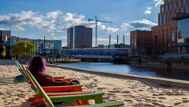 A person sitting in the chairs on the beach at Rotary Park, enjoying the view of Downtown Lansing