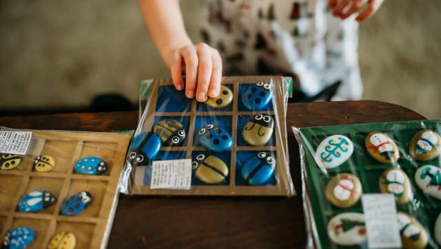 A kid picking up some painted stones that look like blue and gold cute bugs