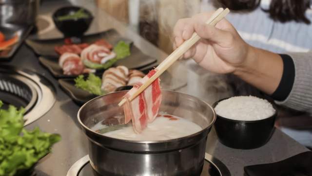 Photo of hand holding chop sticks putting meat into a hot pot with food in the background at KPOT Korean BBQ & Hot Pot.