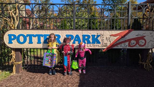 Three kids dressed in halloween costumes in front of the Potter Park Zoo sign
