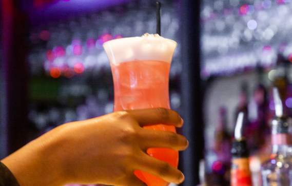 Hand holding a tall pink cocktail in front of the counter at Darryl's Corner Bar and Kitchen