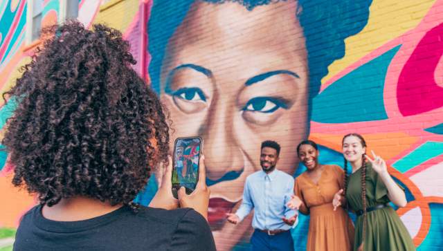 3 Friends Pose in front of Street Art mural while a person takes a photo