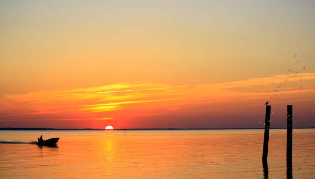 Skiff sailing on reflective river during an orange sunset