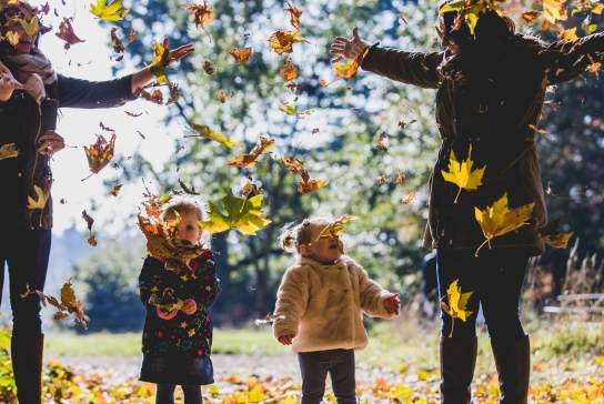 Two mothers and their young daughters throwing fallen leaves in the grounds of Westonbirt Arboretum near Bristol in autumn - credit Johnny Hathaway