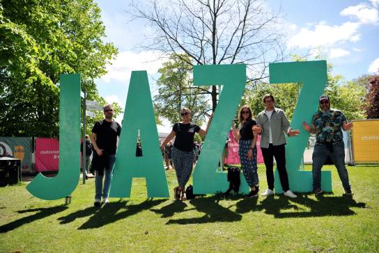 Cheltenham Jazz Festival attendees stood next to a JAZZ sign in Montpellier Gardens, Cheltenham