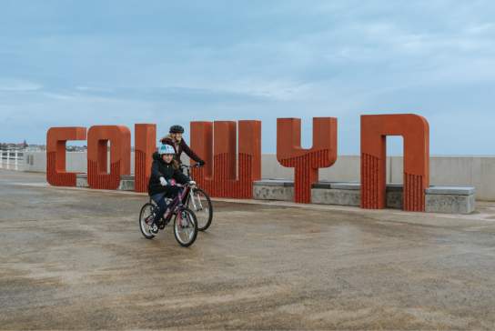 Cyclists going past the Colwyn sign