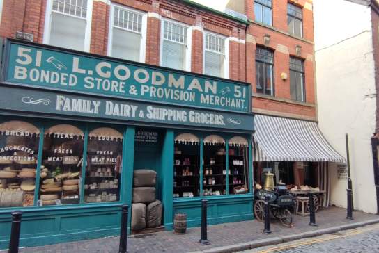 Hullywood film set featuring a vintage storefront for L. Goodman Bonded Store & Provision Merchant, displayed with period crates, produce, and old‑style shop signage along a cobbled street, recreating an authentic historical marketplace atmosphere ideal for film and TV production