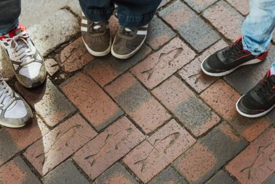 Children standing on brick paving stones engraved with fish designs along Hull’s Fish Trail.