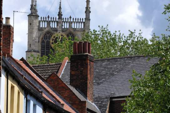 View of Hull Minster rising above historic brick townhouses and rooftops on Prince Street, framed by trees