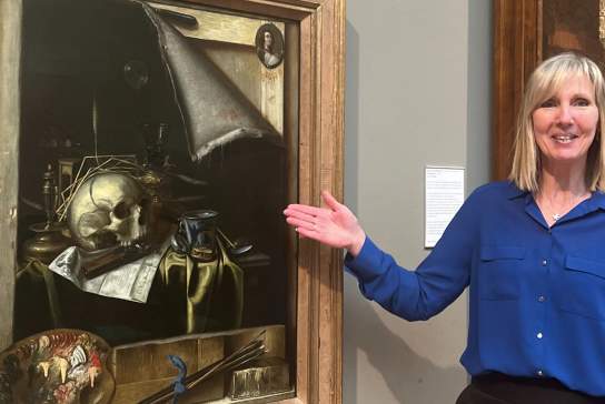 A guide presenting a framed still‑life painting inside Ferens art gallery, Hull, with detailed artwork and exhibition labels visible on the wall.