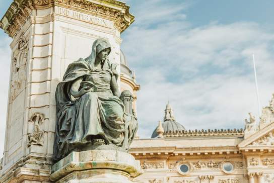 Historic statue seated before ornate classical architecture in Hull’s city centre under a bright sky.