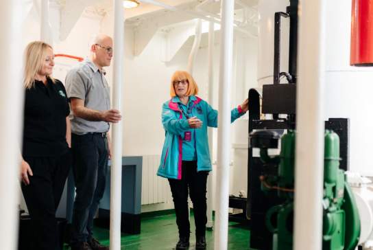 Visitors and a guide inside the engine room of a Spurn Lightship, Hull Marina discussing the machinery and equipment during a tour.