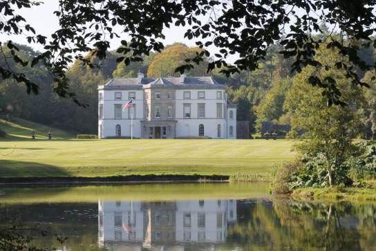 Exterior shot of Montalto House with an American flag on the grass and a lake visible at the front of the shot.