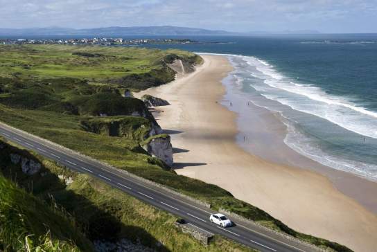 Aerial view of a car along the Causeway Coastal Route on a sunny day with the beach in the background