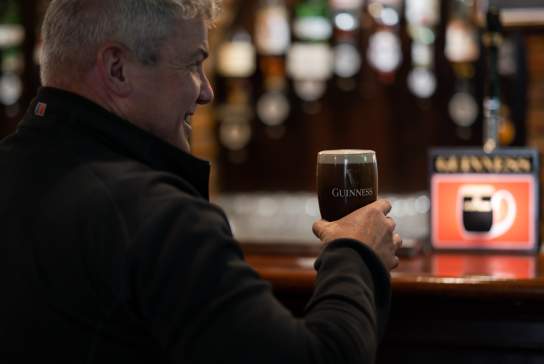 Man enjoying a pint of Guinness at the bar in Charlie's Bar in Enniskillen with optics in the background.