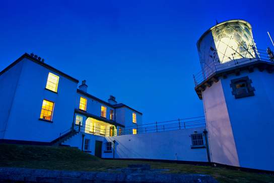 Guest Accommodation at Blackhead Lighthouse in Whitehead. Outside view of Lightkeepers cottage and lighthouse in evening light.