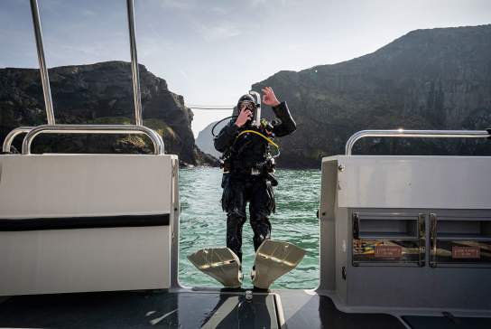 Scuba diver falling backwards from a boat while giving a thumbs up