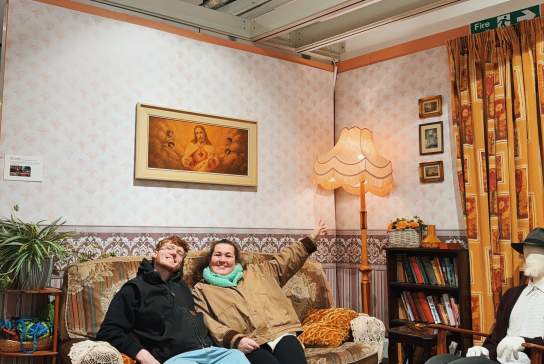 Influencer Sasha Ferg and a friend sitting on a sofa which is part of The Derry Girls Exhibition.