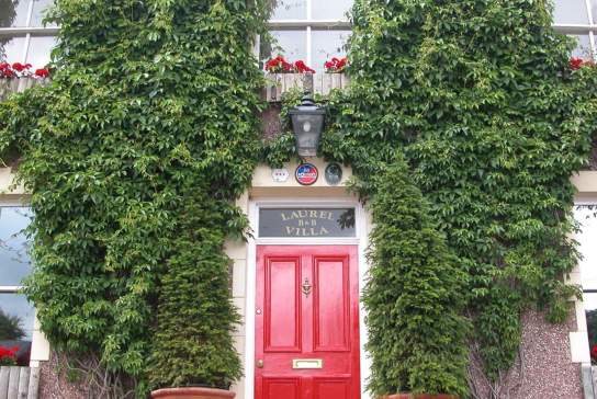 Exterior shot of Laurel Villa showing a red front door and moss on the exterior walls.