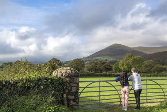 Couple standing at a gate admiring the lush green countryside and mountain in the distance