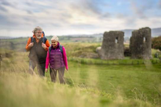 A couple enjoying a walk around the site of Harry Avery's castle with ruins in the background
