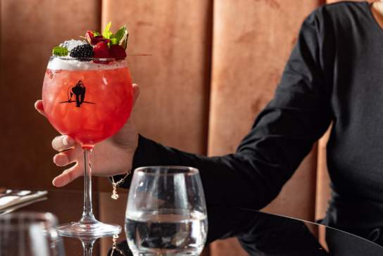 Close up of someone holding a red colour cocktail in a round glass with stem