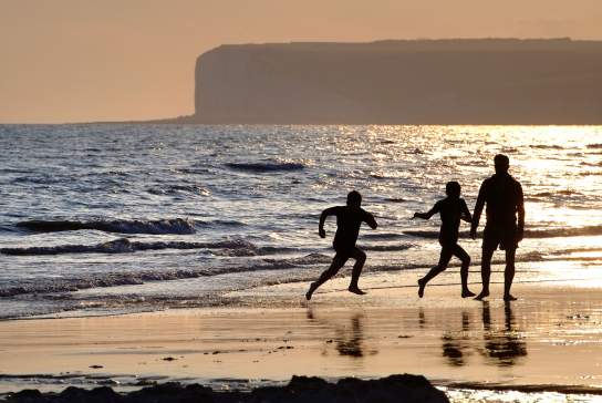 A family playing on the beach at sunset at Birling Gap, Sussex