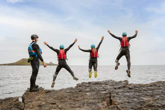 Group of people coasteering and jumping into water while instructor watches on