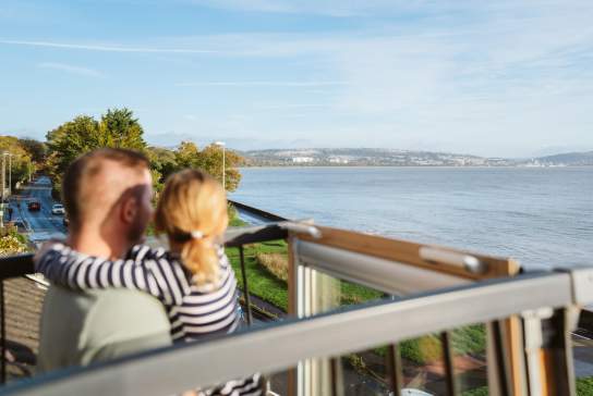 Father and daughter standing on balcony looking out over Swansea Bay