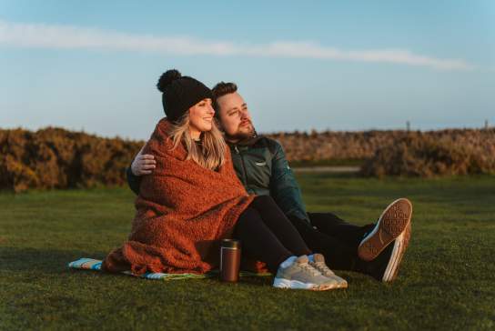 Young couple under a blanket with a coffee watching a sunset at rhossili bay in the winter