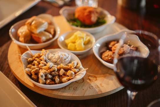 Battered cockles in a bowl with a glass of red wine.