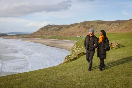 Couple walking along rhossili bay coastline