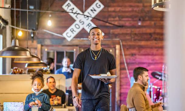 Male server at a restaurant walking holding a plate of food