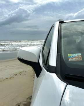 White car on the beach with a parking pass on the window for 2024