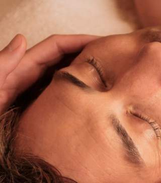 A person lays on a cloth table with a set of hands massaging their head