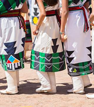 A group of individuals stand closely together, wearing colorful traditional indigenous clothing