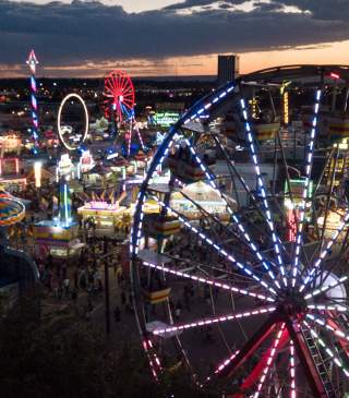 An aerial view of a colorful Ferris wheel in the foreground with other colorful amusement rides in the background
