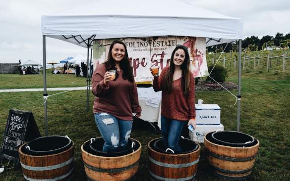 Two women in half barrels holding glasses toast to the grape harvest at Folino Estate Winery.